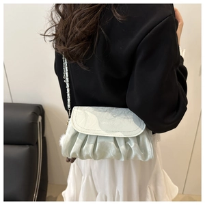 Detail of mint green ruched crossbody bag with silver chain strap worn by a model