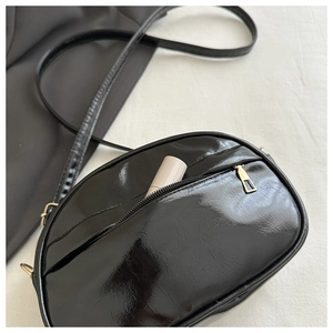 Detail of glossy black mini crossbody bag with golden zipper and lipstick inside pocket