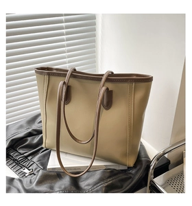 Detail of a beige tote bag with brown handles placed on a black leather jacket and book