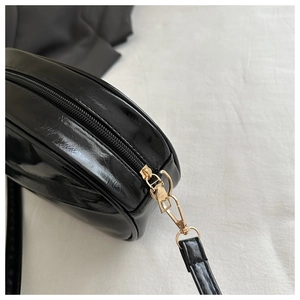 Detailed macro view of black glossy leather bag surface with golden zipper and strap clip