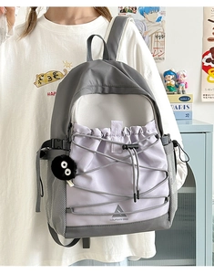 Detail of grey and purple canvas backpack featuring drawstring pocket and plush charm
