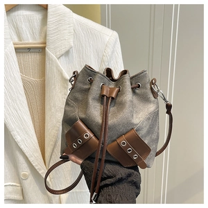 Detail of grey denim bucket bag featuring brown leather trim and silver metal eyelets
