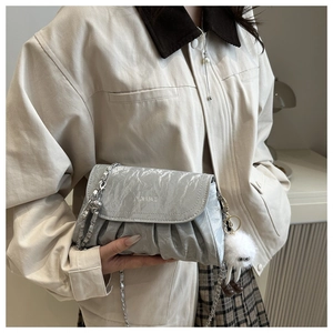 Detail of silver pleated crossbody bag with metal chain and white plush ball charm