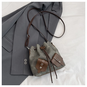 Detail of grey canvas bucket bag with brown leather trim and drawstring closure