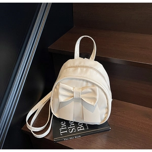 Detail view of cream mini backpack featuring a large decorative bow and matte PU leather