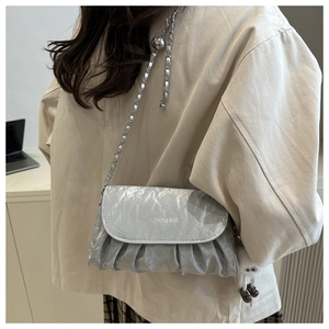Detail of silver pleated crossbody bag with chain strap and plush ball charm accessory