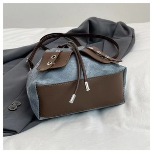 Detail of drawstring bucket bag made of light blue denim and brown leather with metal eyelets