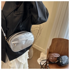 Close-up of metallic faux leather crossbody bag with oval shape and dual zipper detail