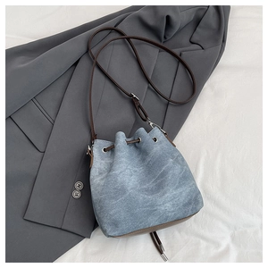 Detailed close-up of a blue denim drawstring bucket bag with premium brown leather accents
