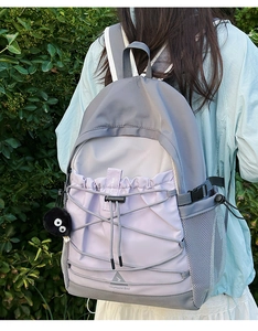 Detail of grey-purple nylon backpack with elastic drawstrings and plush monster charm