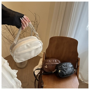 Detailed view of white, brown and black PU leather crossbody bags on a wooden chair