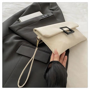 Detail view of a minimalist cream envelope clutch bag with black square buckle on a suit