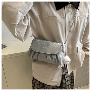 Detail of silver pleated crossbody bag with chain strap and cute plush charm on a model