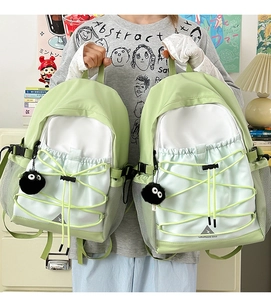 Detail of mint green and white canvas backpack featuring decorative elastic cords and side pockets