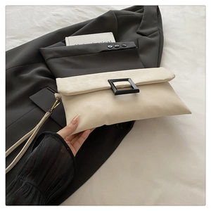 Detail of a beige PU leather envelope clutch with a black square clasp and wrist strap