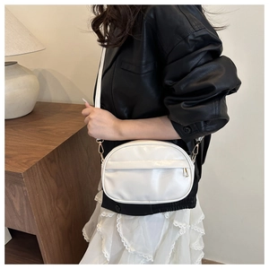 Detailed close-up of a white leather shell crossbody bag with fine texture and golden hardware