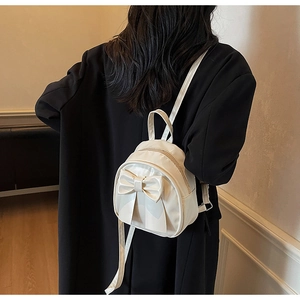 Rear view of a cream mini backpack with a large bow detail on a black coat outfit