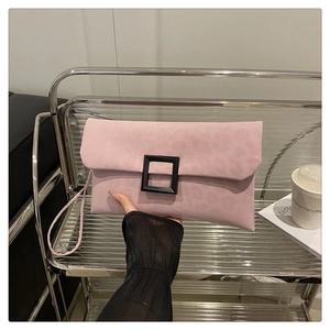 Close-up of pink suede envelope clutch bag featuring a modern black square buckle detail