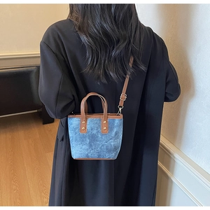 Détail d'un sac seau en denim bleu avec bordures en cuir marron et rivets en métal