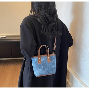 Détail d'un mini tote en denim bleu avec lanières en cuir marron sur manteau noir