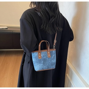 Sac cabas bleu avec poignées en cuir marron et rivets dorés porté par un mannequin en manteau noir