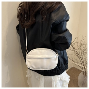 Detail of white glossy crossbody bag with gold hardware worn by a model in black leather jacket