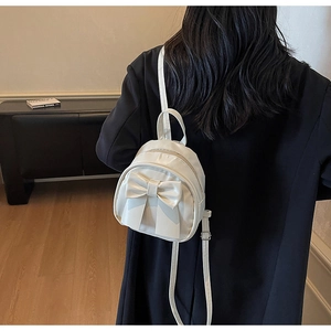 Detail view of mini white bow backpack showing soft glossy PU leather and strap on model