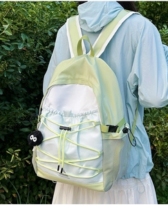 Detail of color-block canvas backpack with lime green drawstrings and plush sprite charm