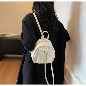 Detail of a creamy white mini PU leather backpack with a bow, worn by a model over a black coat