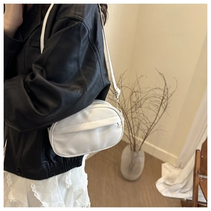 Detail view of a white oval crossbody bag in PU leather worn by a model in lifestyle setting