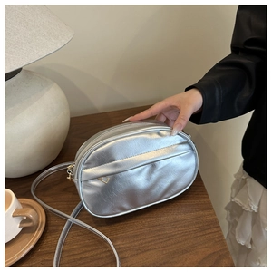 Detailed view of silver metallic oval crossbody bag with pleated texture on wooden table