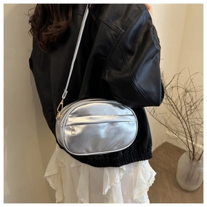 Detail of silver oval crossbody bag with fine texture and adjustable strap on a model