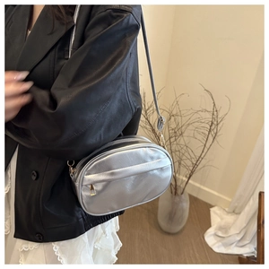 Silver shell-shaped crossbody bag with metallic finish shown on model in minimalist setting