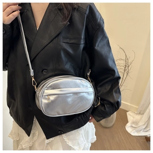 Close-up of a metallic silver crossbody bag with a minimalist oval design on a leather jacket