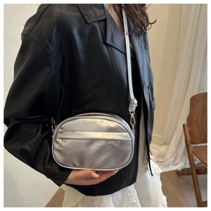 Detail of silver oval crossbody bag with smooth metallic finish and gold zipper hardware