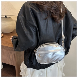 Silver oval crossbody bag in shiny metallic leather with gold zipper worn by model