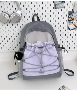 Detailed view of canvas backpack with grey and lavender color-block and bungee cord detail