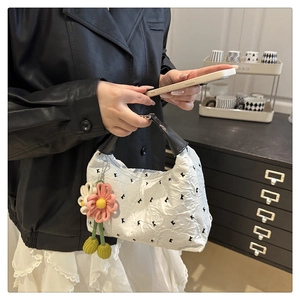 Détail du sac plissé blanc avec broderie de lettres et pendentif fleur en tricot