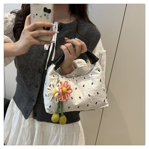 Détail du sac à main plissé blanc avec poignées noires et charm floral marguerite