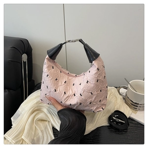 Détail du sac à main rose clair avec imprimés K noirs et bandoulière sur tissu blanc plissé