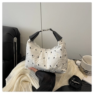 Détail d'un sac en tissu plissé blanc avec broderies et poignée en cuir sur canapé