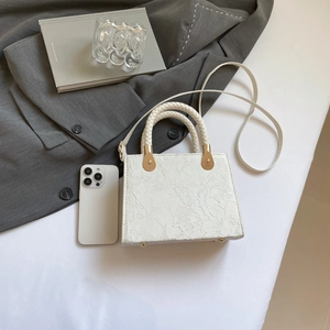 White lace texture crossbody bag with woven handle and gold hardware on a desk