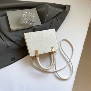 Detail of white rectangular handbag with embossed floral texture and woven handle