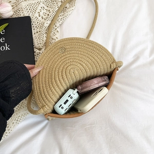 Beige round straw crossbody bag with metal buckle shown with phone and power bank