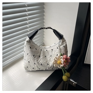 Détail du sac à main plissé blanc avec breloque fleur et poignée noire large