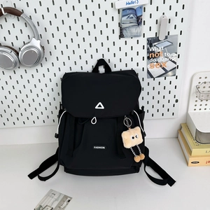 Detail view of black hiking backpack with white cord toggles and a plush charm accessory