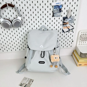 Detail of light gray nylon backpack featuring drawstring closure and yellow plush charm