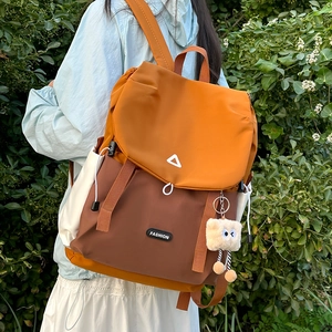 Outdoor shot of an orange and brown color-block backpack with fuzzy monster charm
