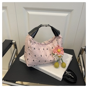 Détail d'un sac à main rose plissé avec anse en cuir noir et breloque fleurie