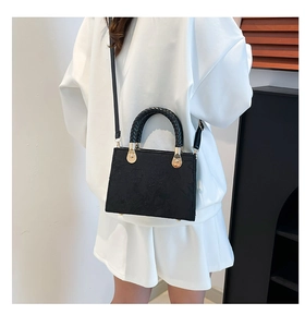 Detail of black tote bag featuring unique circular woven handle and gold hardware accents